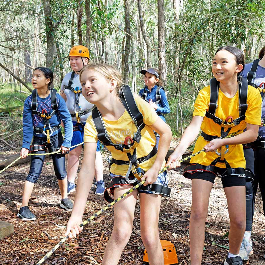Group of children in safety gear engaging in a school camp team-building activity in a forest.