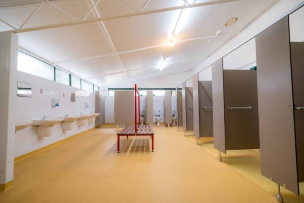 Interior of a bright, clean public restroom with multiple stalls, sinks, and a red stepladder in the center.