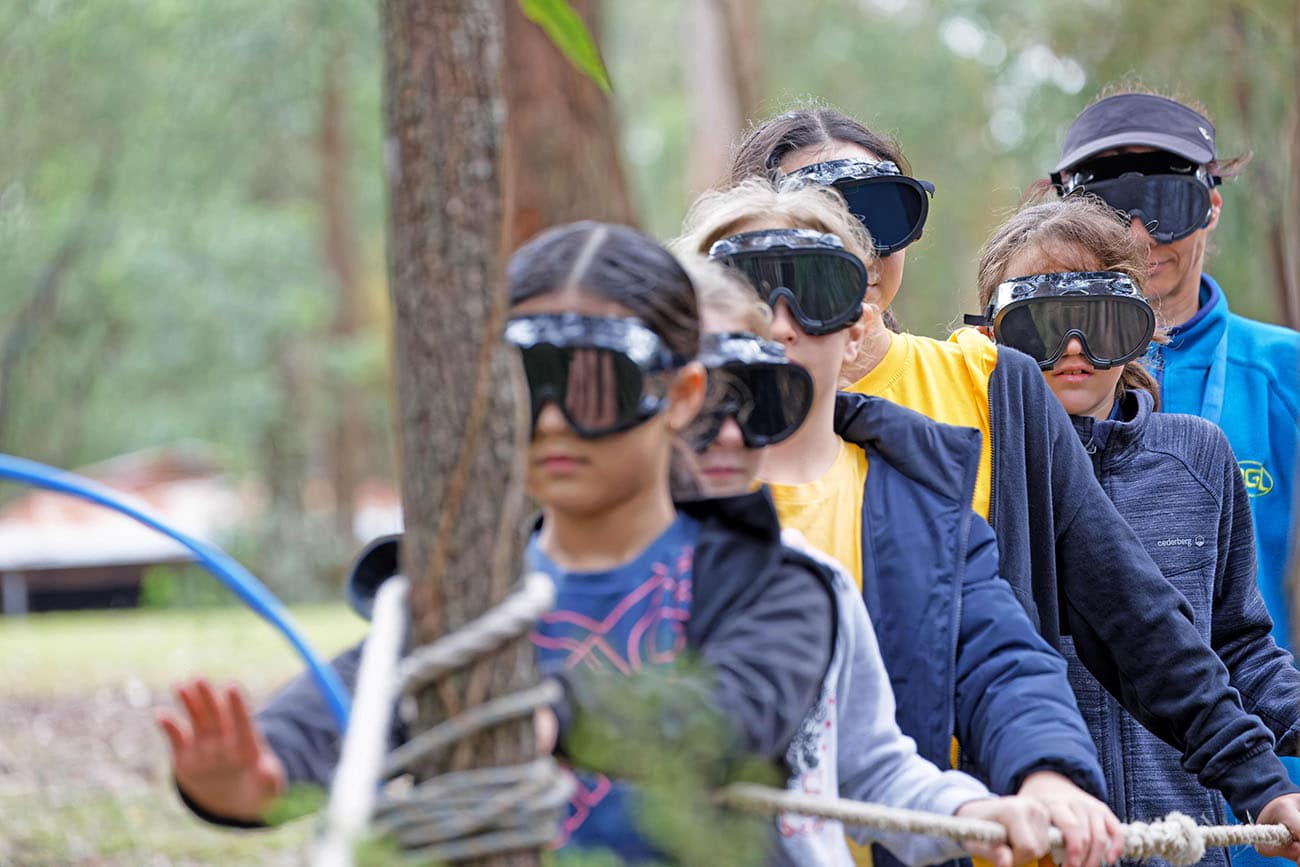 A group of children and adults wearing VR headsets discover an outdoor activity in a wooded area.