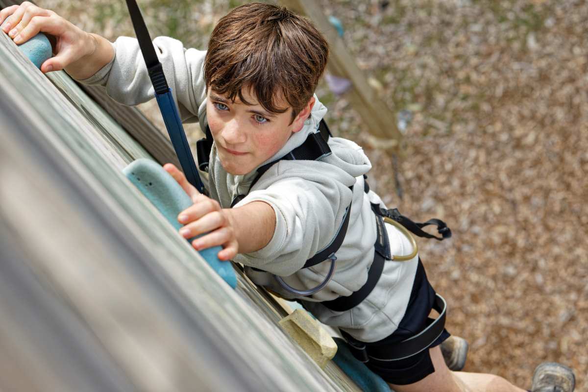 A young boy climbing a rock wall, focused and holding onto a grip, wearing a harness and helmet, united with his challenge.