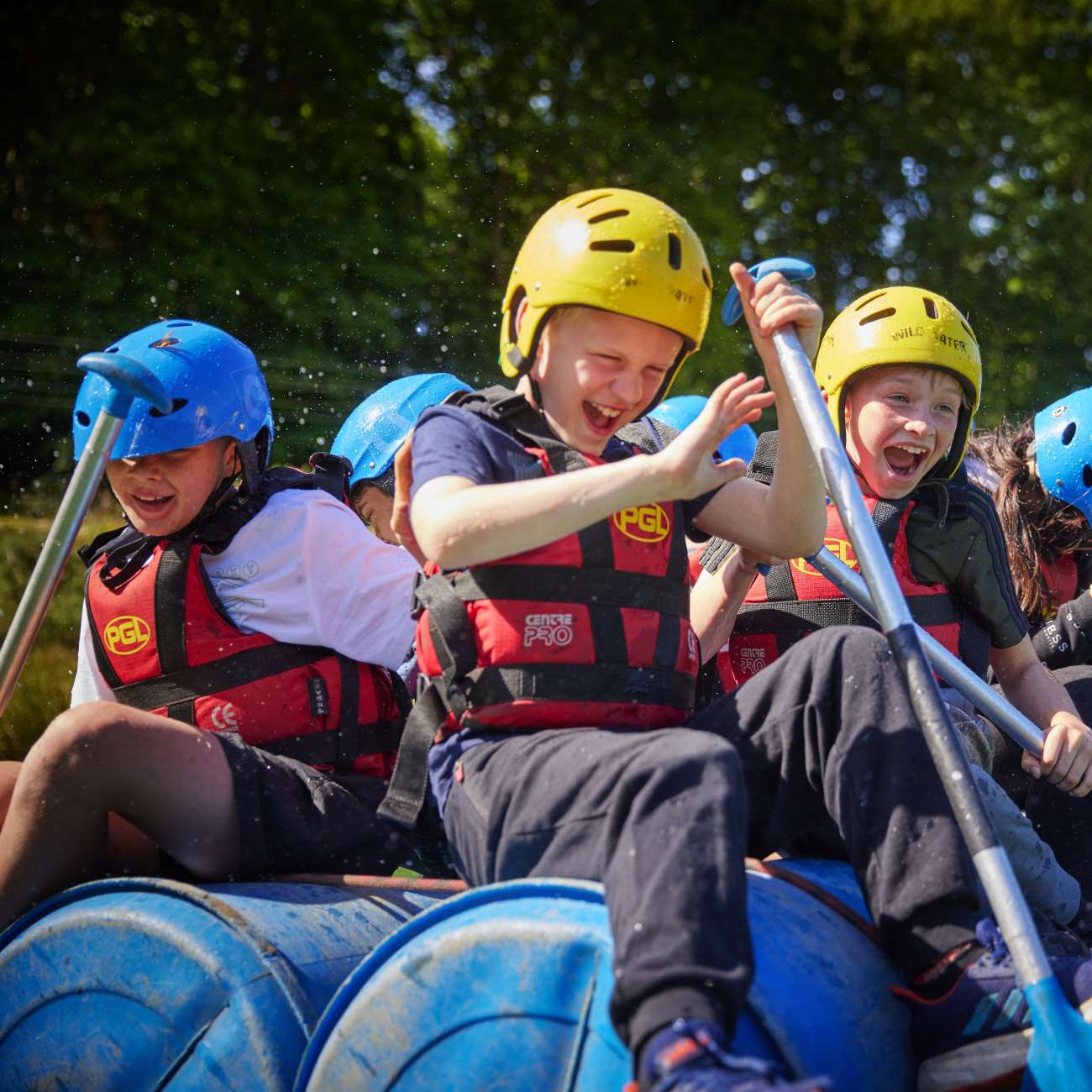 Group of children wearing helmets and life vests, laughing while rafting and discovering nature on a sunny day.
