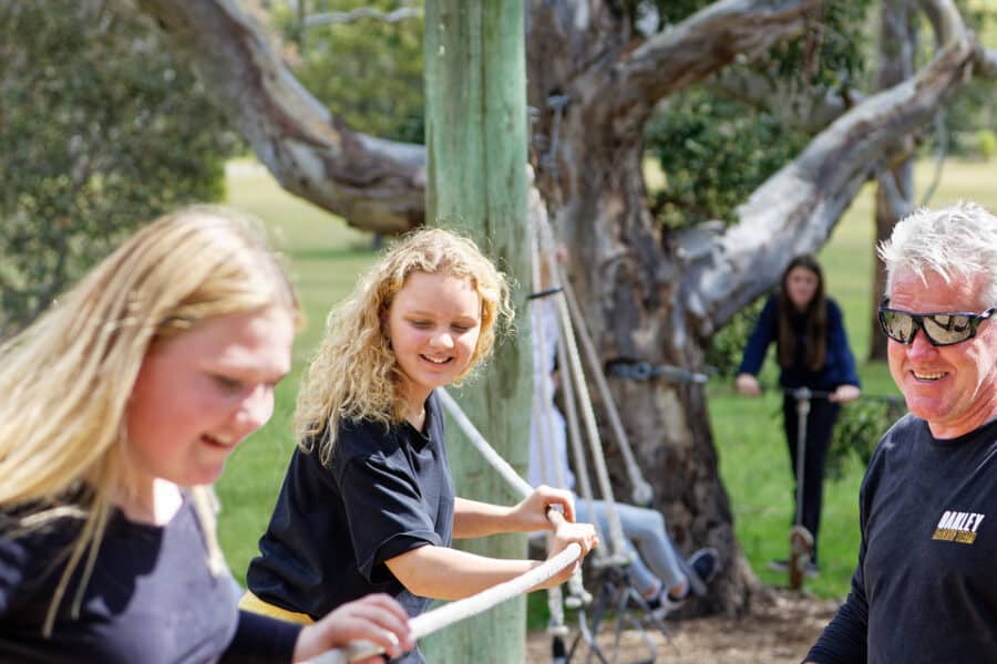 Three people enjoying an outdoor activity in a park, two smiling women and an older man engaging in playful interaction.