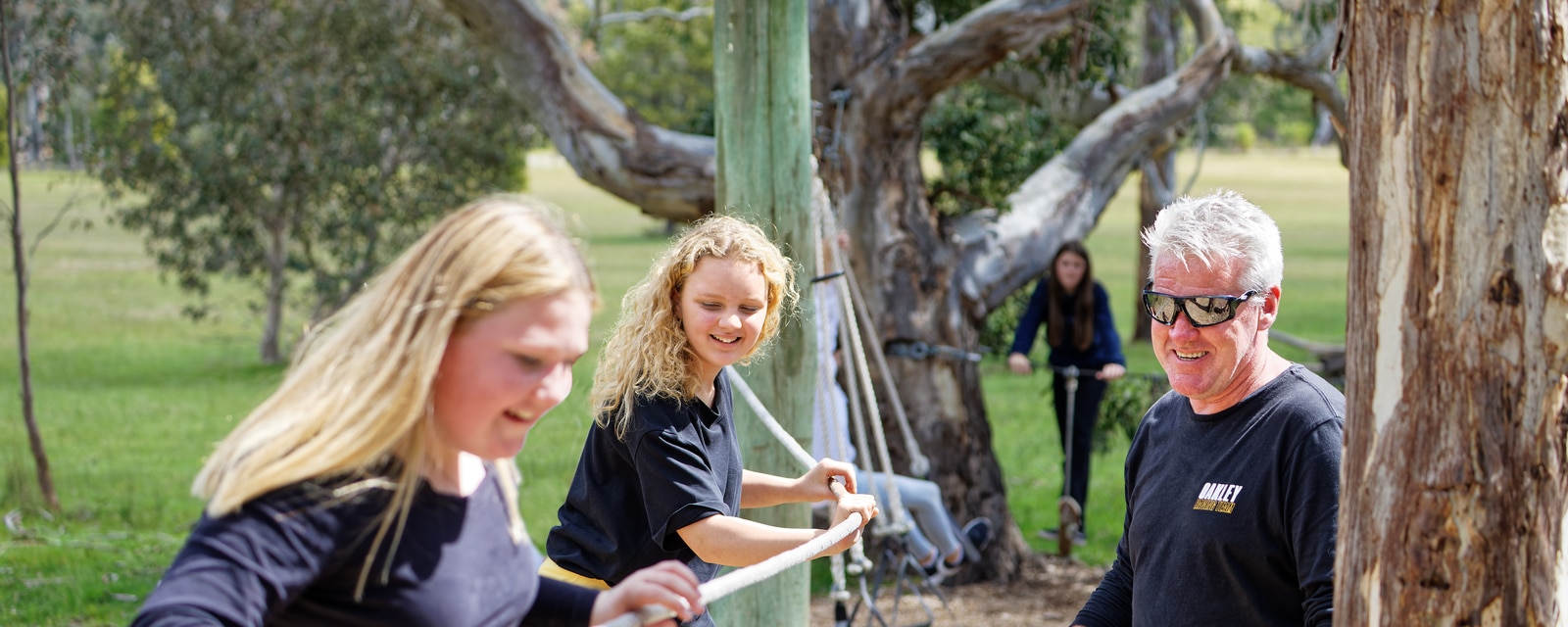 Three people enjoying an outdoor activity in a park, two smiling women and an older man engaging in playful interaction.