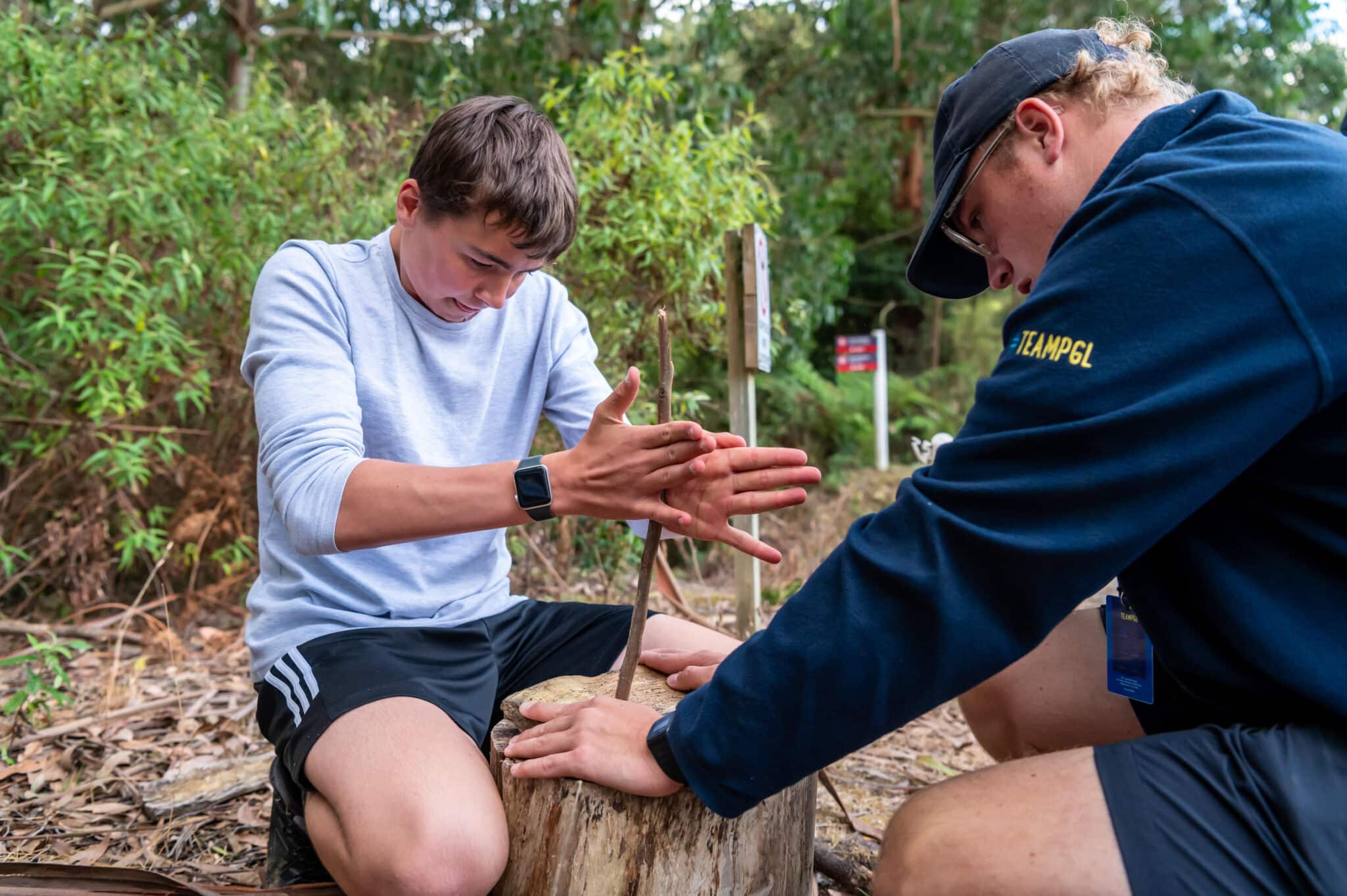 Two young men in casual sportswear discover each other's strength in a friendly arm wrestling match on a log outdoors.