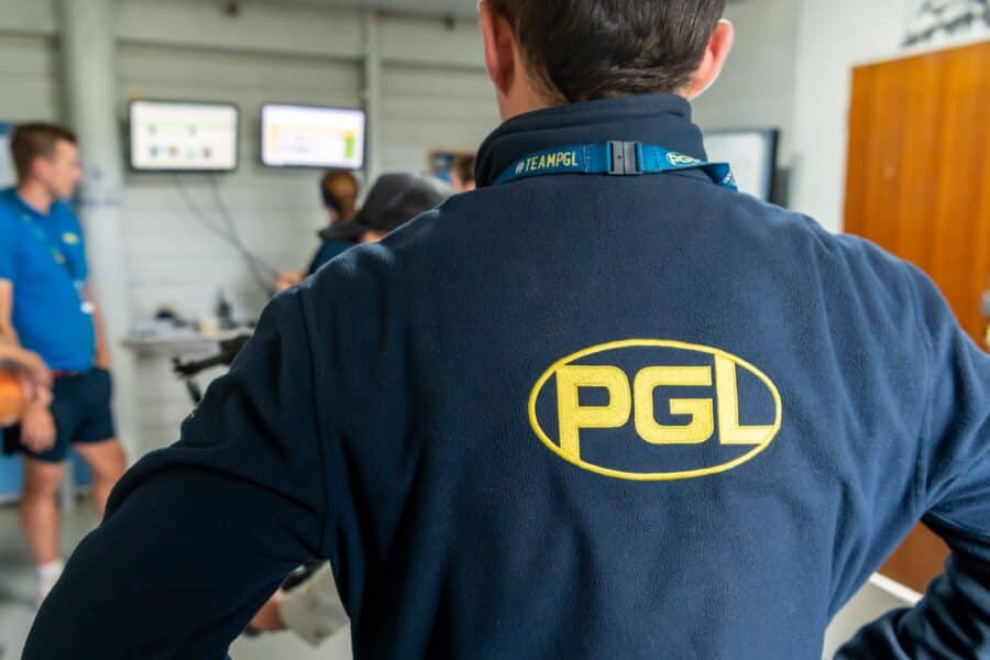 A person in a "PGL" jacket faces a group of three people in a room with screens on the wall.